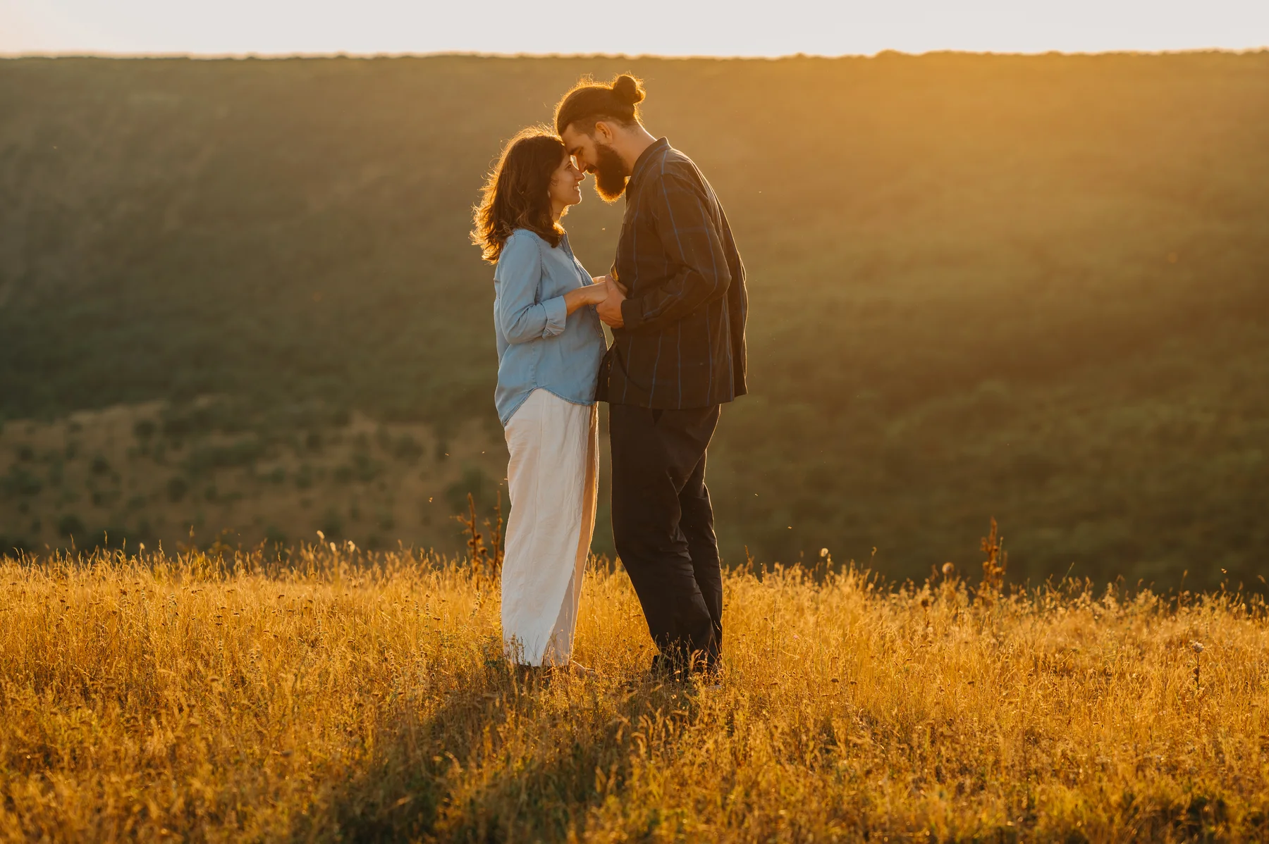 A couple standing forehead to forehead in a golden field at sunset